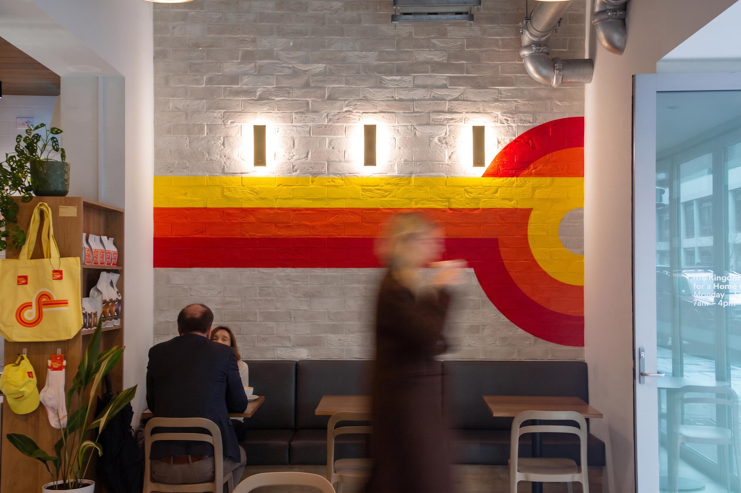 The Pirie Street dining room with a striped mural on the brick wall behind the booth seating and retail shelf
