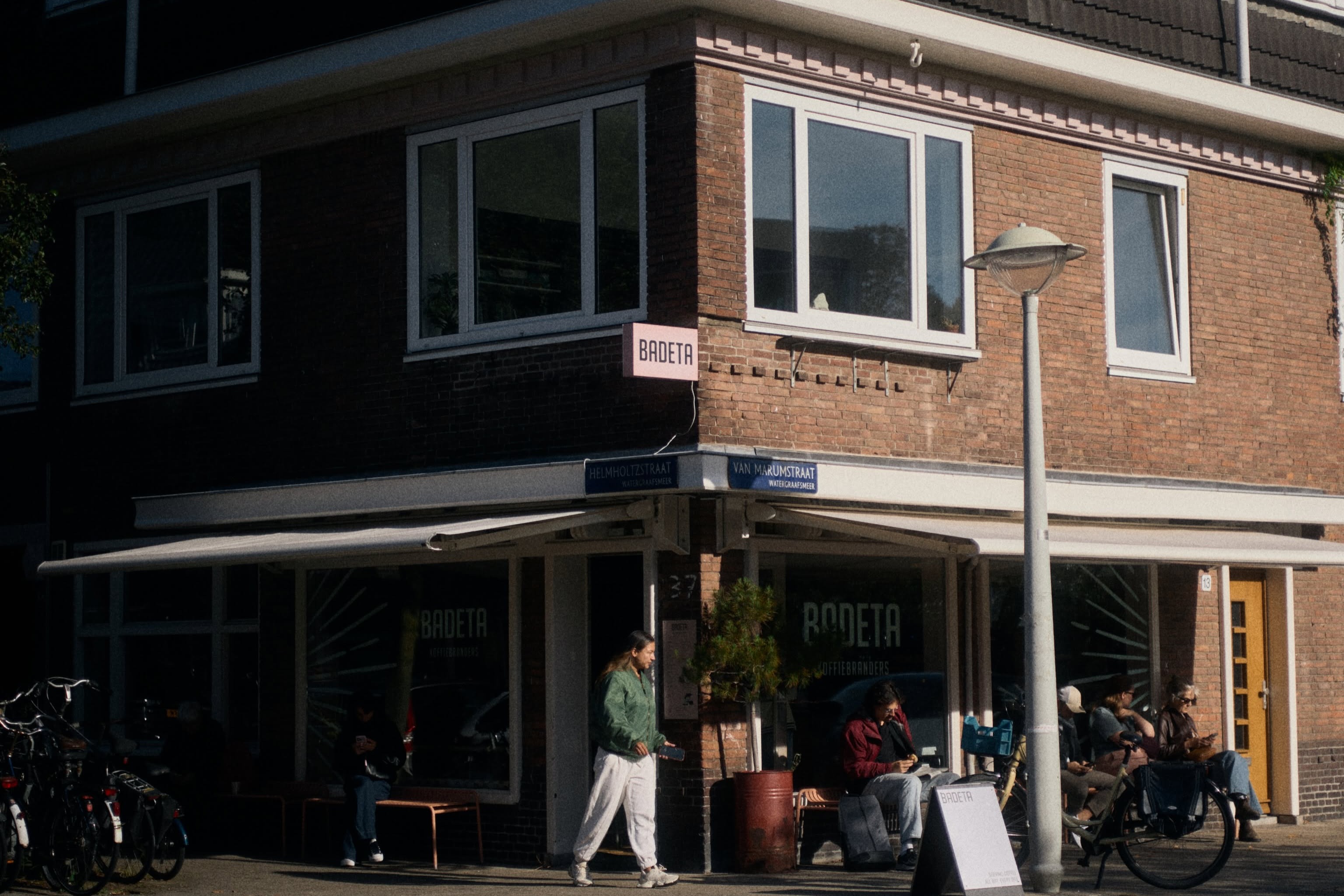 The Badeta storefront on the Helmholtzstraat and Van Marumstraat corner, pink BADETA sign above the awning and outdoor seating out front
