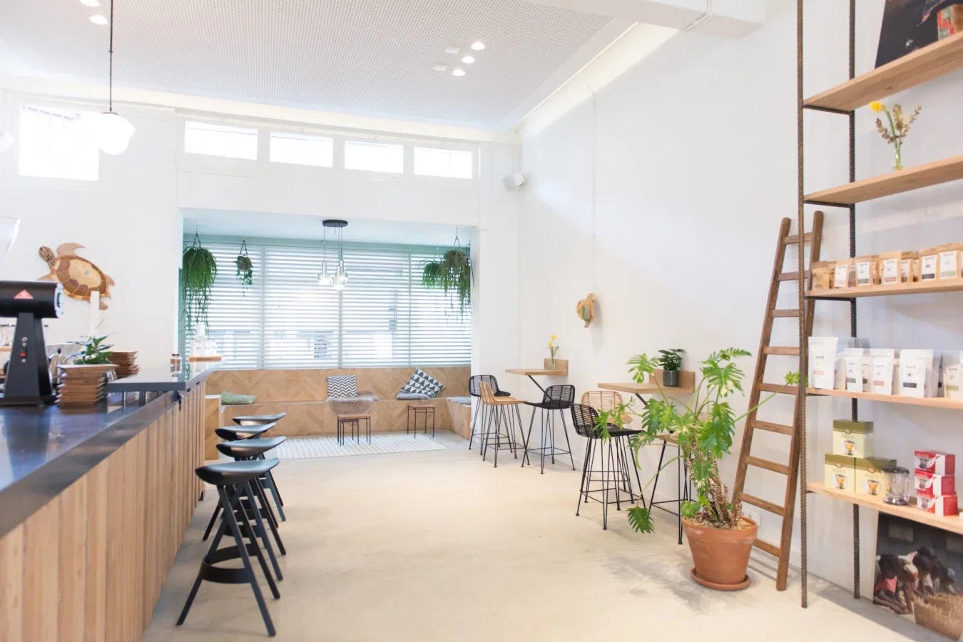 The bright Kerkstraat showroom, wooden counter and bar stools beside a window seat, ladder shelving stocked with retail bags