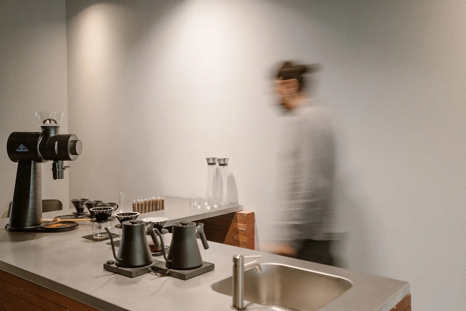The pour over bar at Elevate Coffee Lab, kettles and drippers on the counter with a bean sample rack, staff walking past a plain white wall