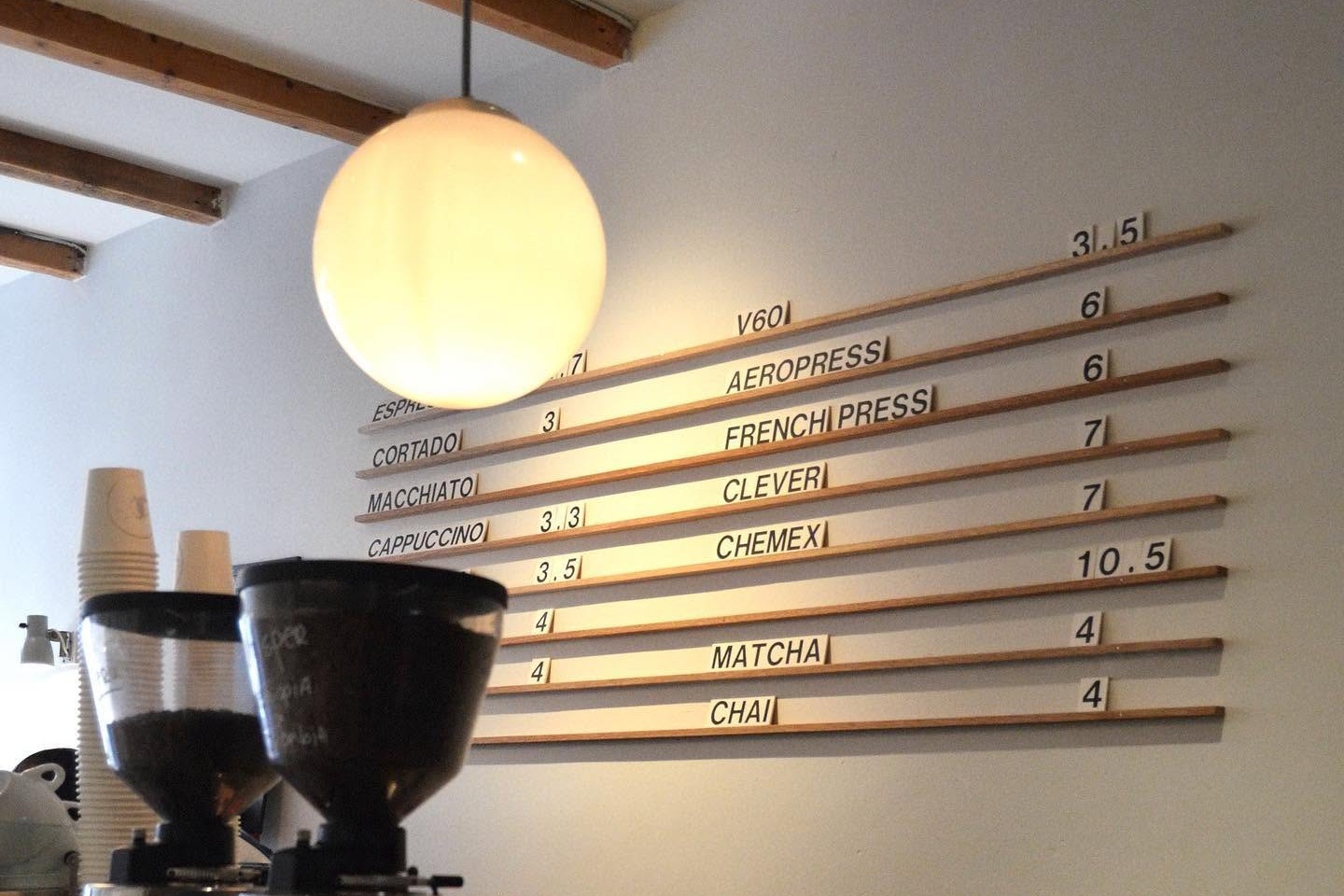 Screaming Beans' wooden menu board listing drinks and prices under a globe pendant light, grinders on the counter below