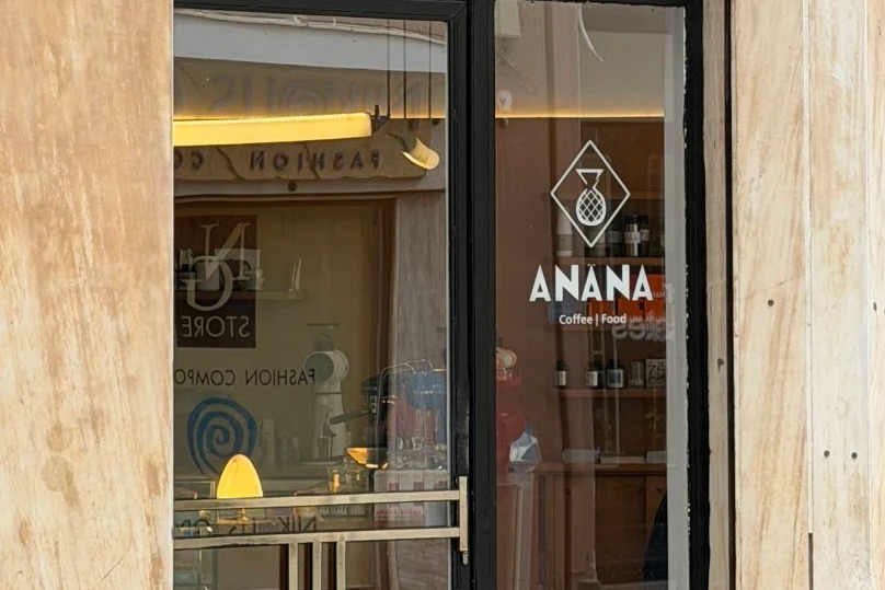 The ANANA Coffee and Food storefront doorway on Praxitelous street, with the shop's pineapple logo etched on the glass