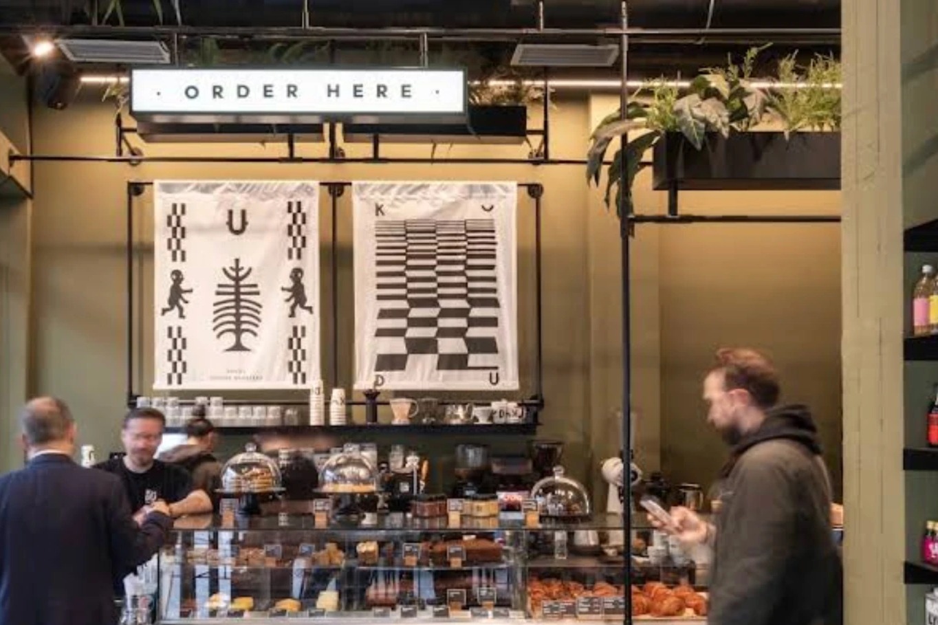 The Kudu counter beneath an ORDER HERE sign and branded wall tapestries, with a pastry case full of cakes and croissants