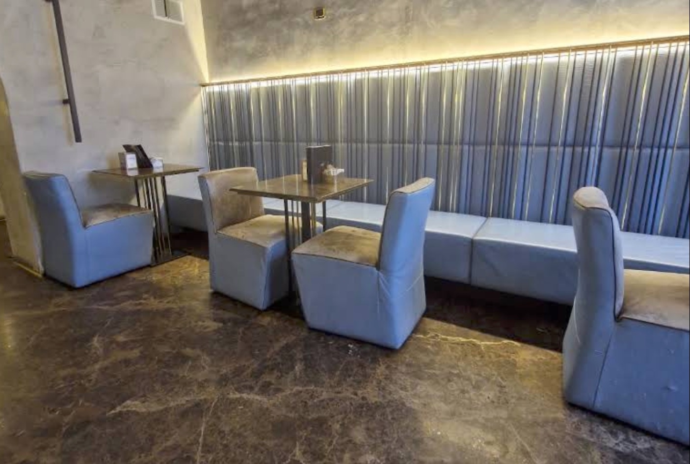 Blue velvet armchairs and a banquette seating area at Veronero, backlit brass panel wall behind