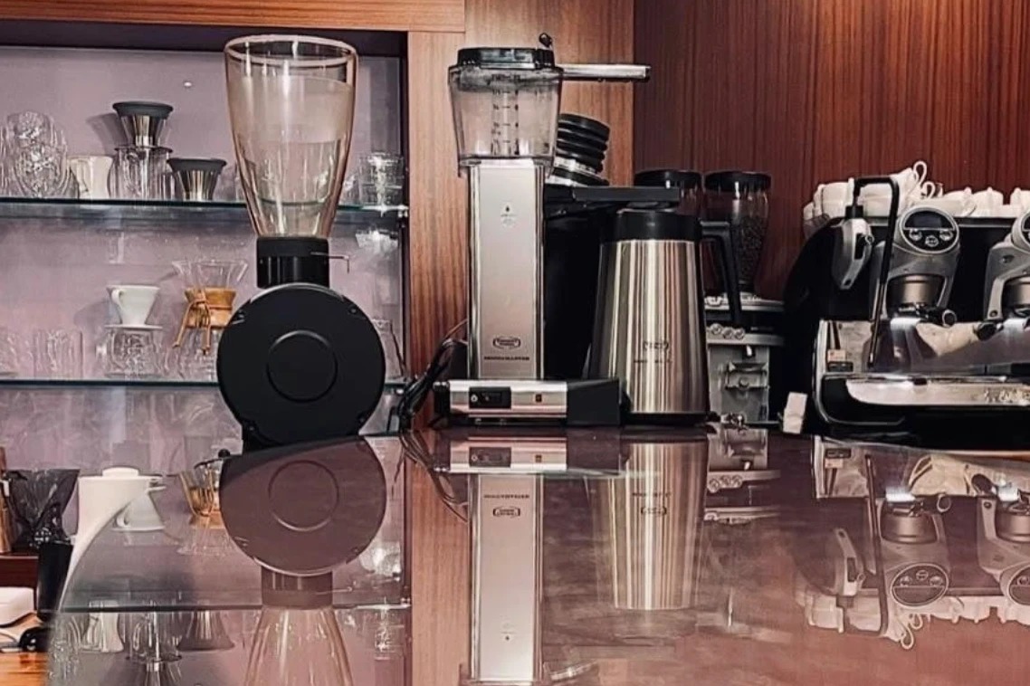 The polished Aroma counter and glass shelving of pour over gear, grinders, and a two group espresso machine reflected on the surface