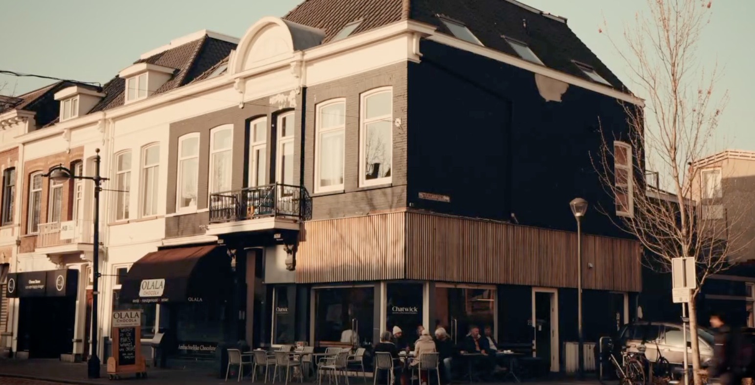 The corner storefront of Chatwick Coffee Roasters on Nieuwe Ginnekenstraat, with outdoor seating and the converted kiosk's dark facade and wood cladding