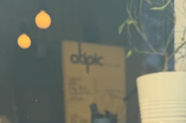 Atipic's storefront window at dusk, showing a menu board, a potted plant and string lights through the glass