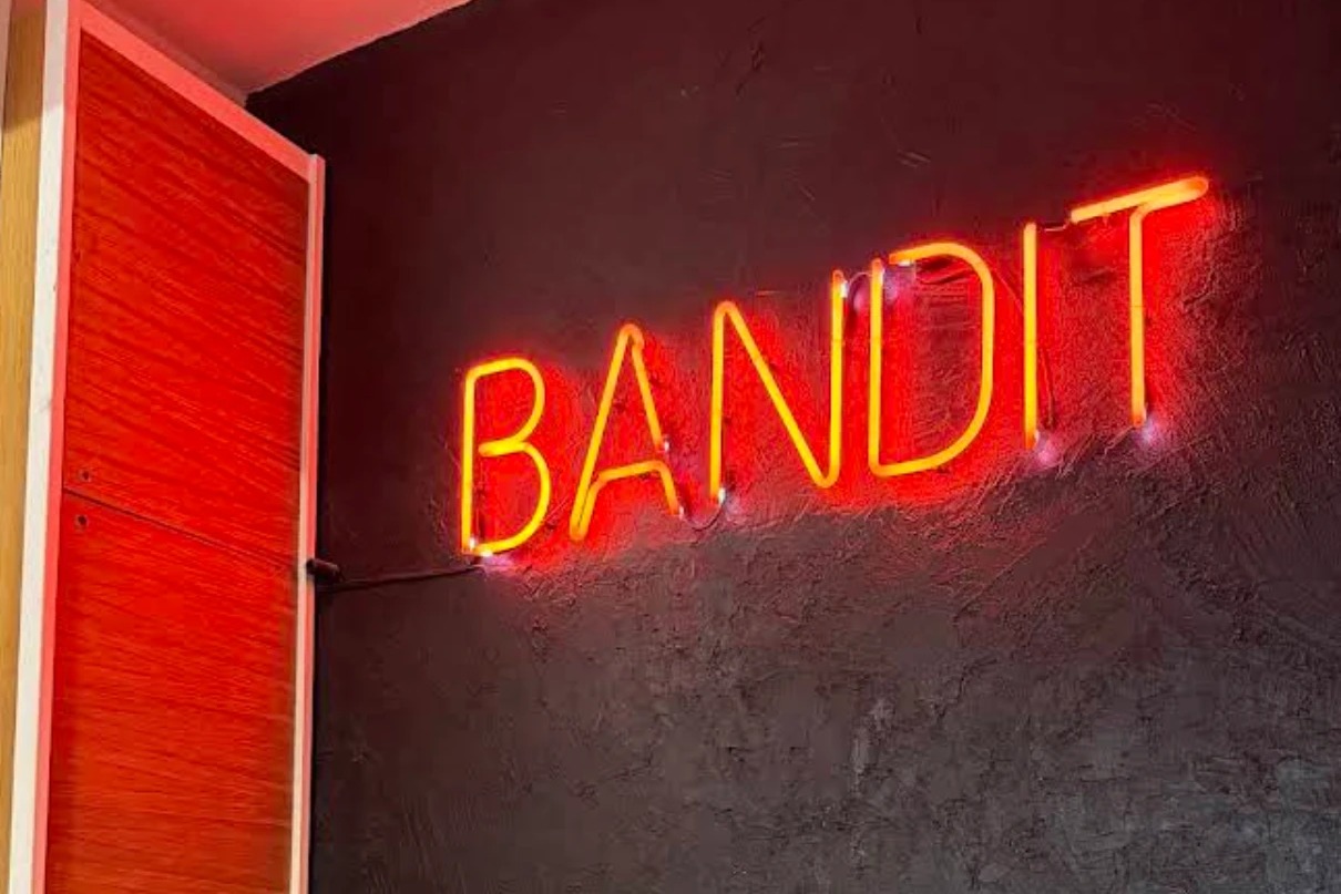 The neon BANDIT sign glowing on a dark textured wall beside the shop's red front door