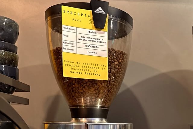 A glass bean hopper with a yellow tasting card reading Ethiopia Guji Mudole, listing producer, tasting notes, altitude and process, roasted by Garage Roastery