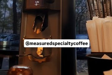 A single dose espresso grinder and dosing cup at Measured's counter, with a window view of the street behind