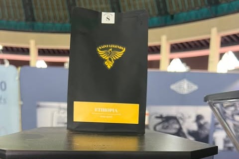 A black Saint Roastery retail coffee bag labeled Ethiopia held up at an outdoor festival stand