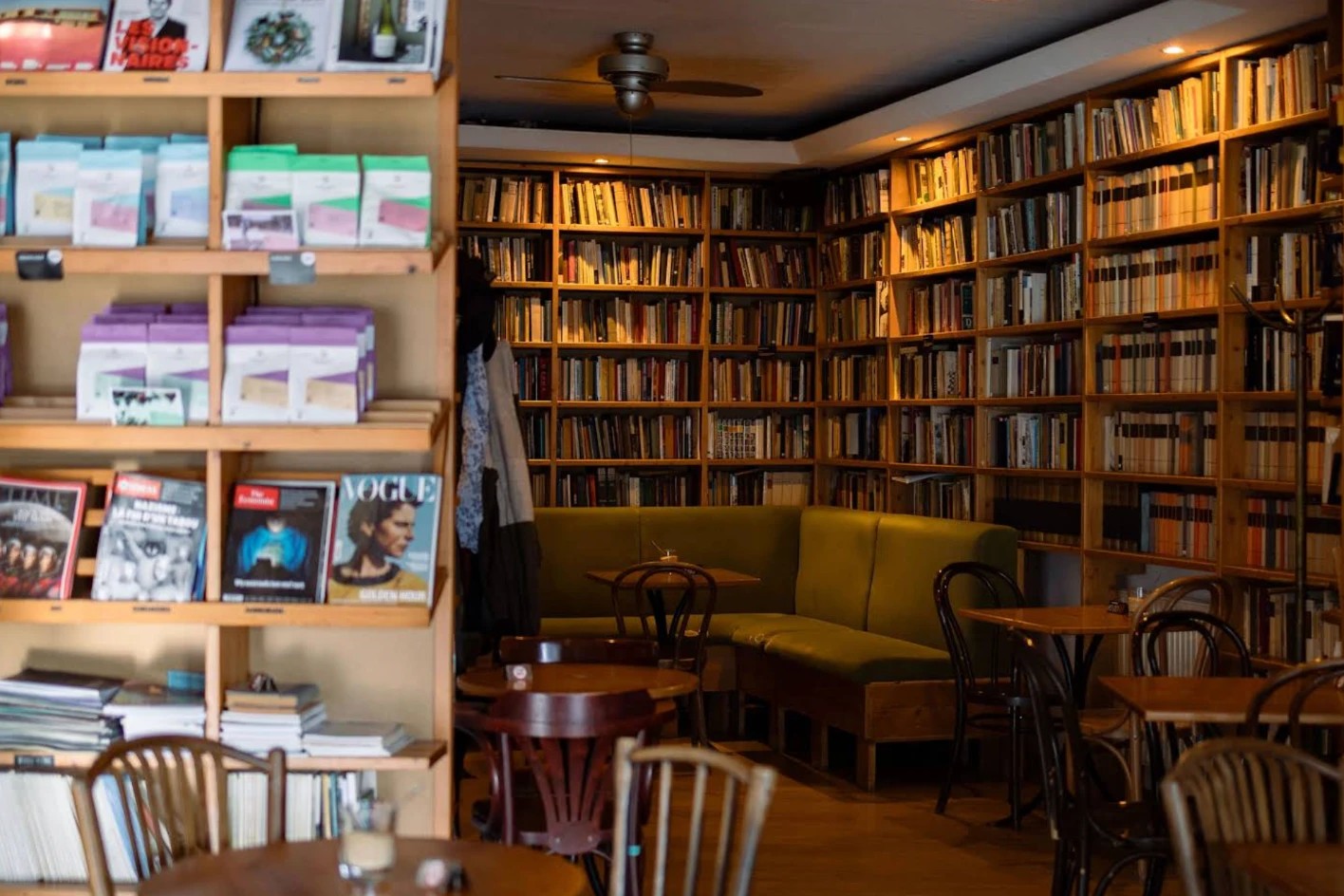 Kelet Kávézó's book lined interior, floor to ceiling shelves packed with volumes, a magazine display in the foreground and a green banquette seating area