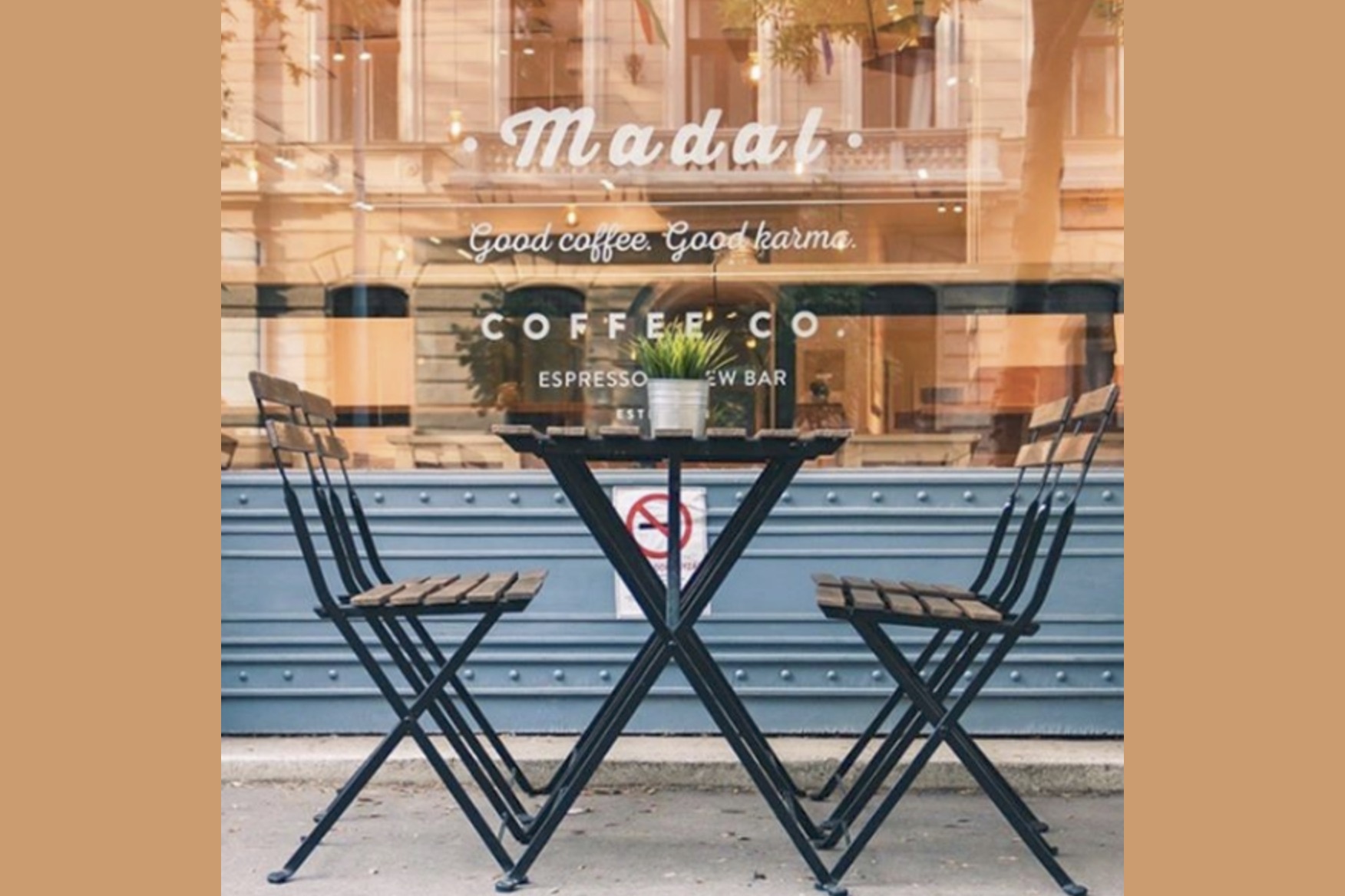 Bistro table and chairs outside Madal Café, the Good coffee, good karma window lettering visible behind