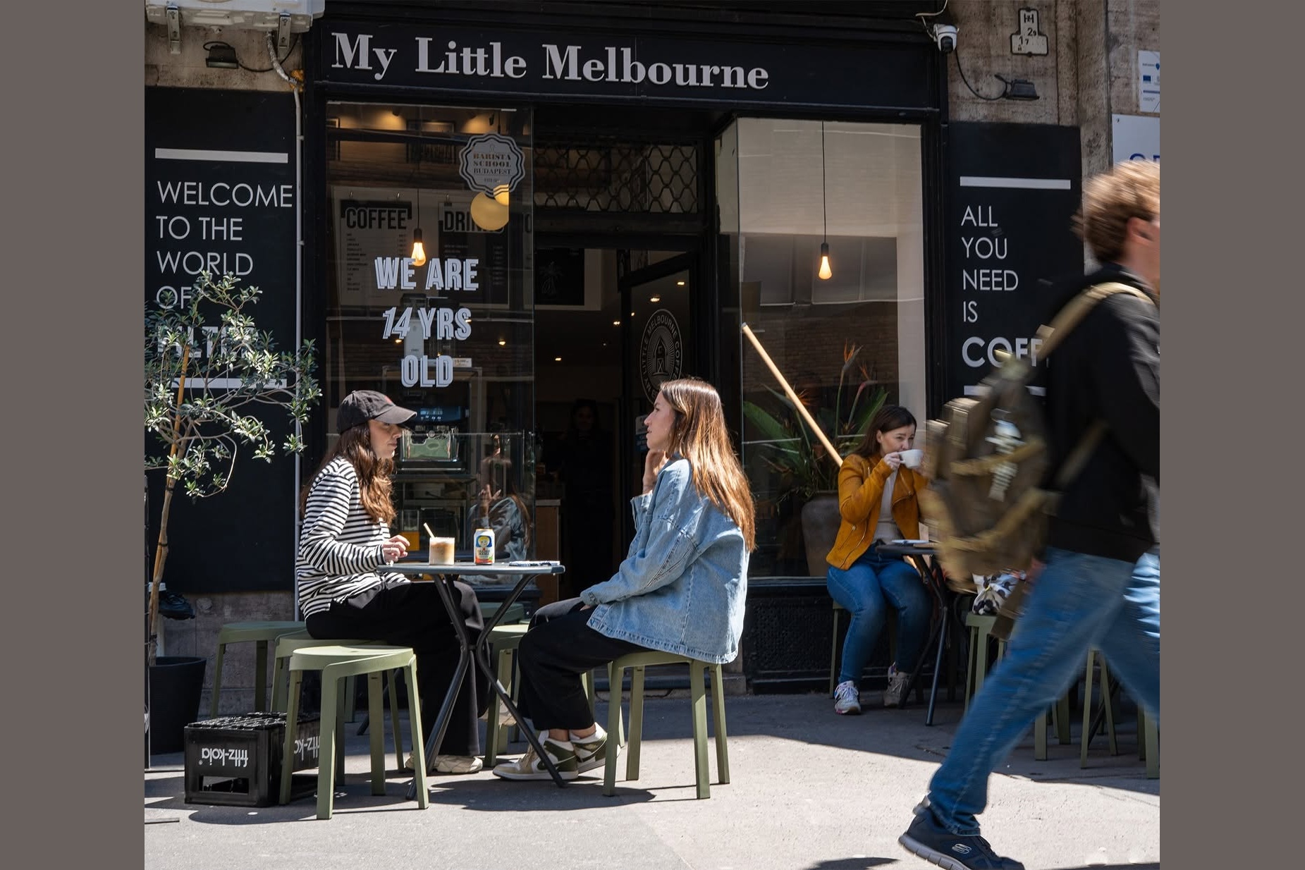 The sidewalk terrace outside My Little Melbourne, a WE ARE 14 YRS OLD sign in the window behind