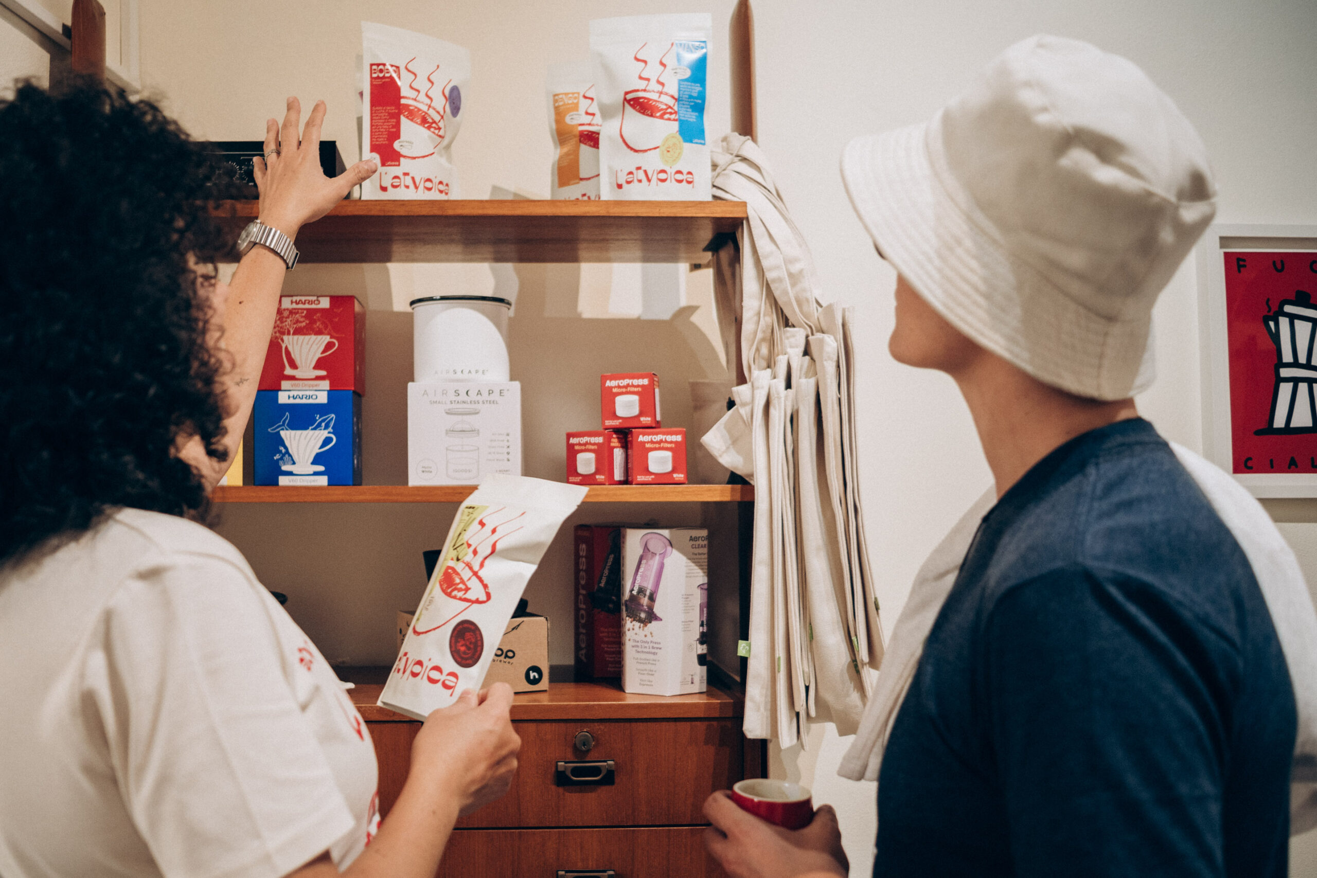 Retail shelves at L'Atypica stocked with branded coffee bags, V60 drippers, AeroPress boxes and canvas tote bags