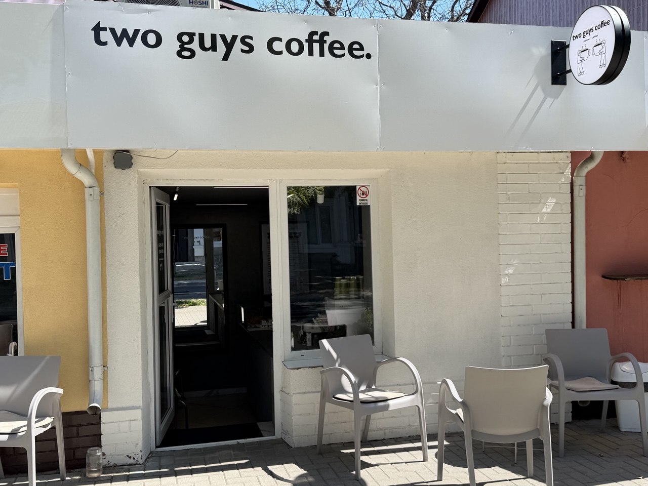 The black storefront facade of two guys coffee with outdoor seating on the pavement
