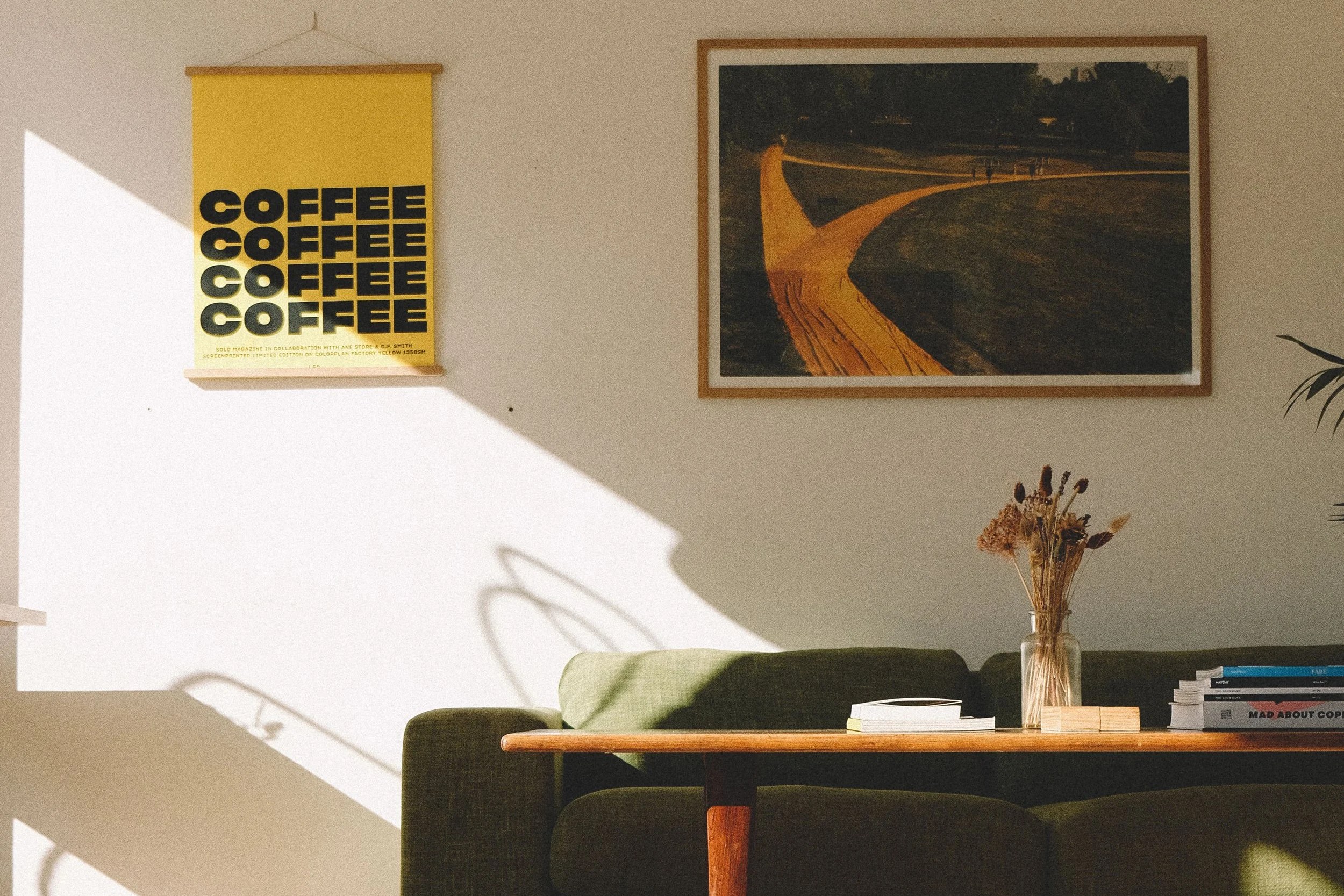 A sunlit corner of Darcy's Kaffe, a green sofa and coffee table beneath a framed print and a yellow COFFEE poster