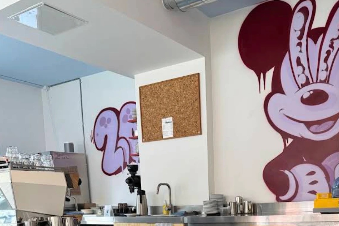 The espresso bar at HipHop with a grinder, pastry rack and a maroon Mickey Mouse mural on the wall above the counter