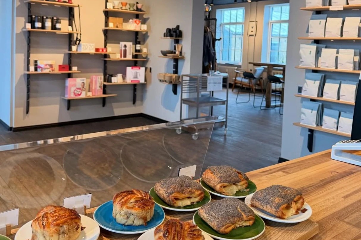 Kaffedepartementet's pastry case in the foreground, shelves of retail bean bags and brewing gear along the walls behind