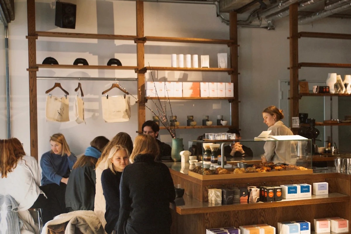 The wood-framed La Cabra counter at Møntergade inside Another Aspect, customers seated at the bar beside a pastry case and retail shelves