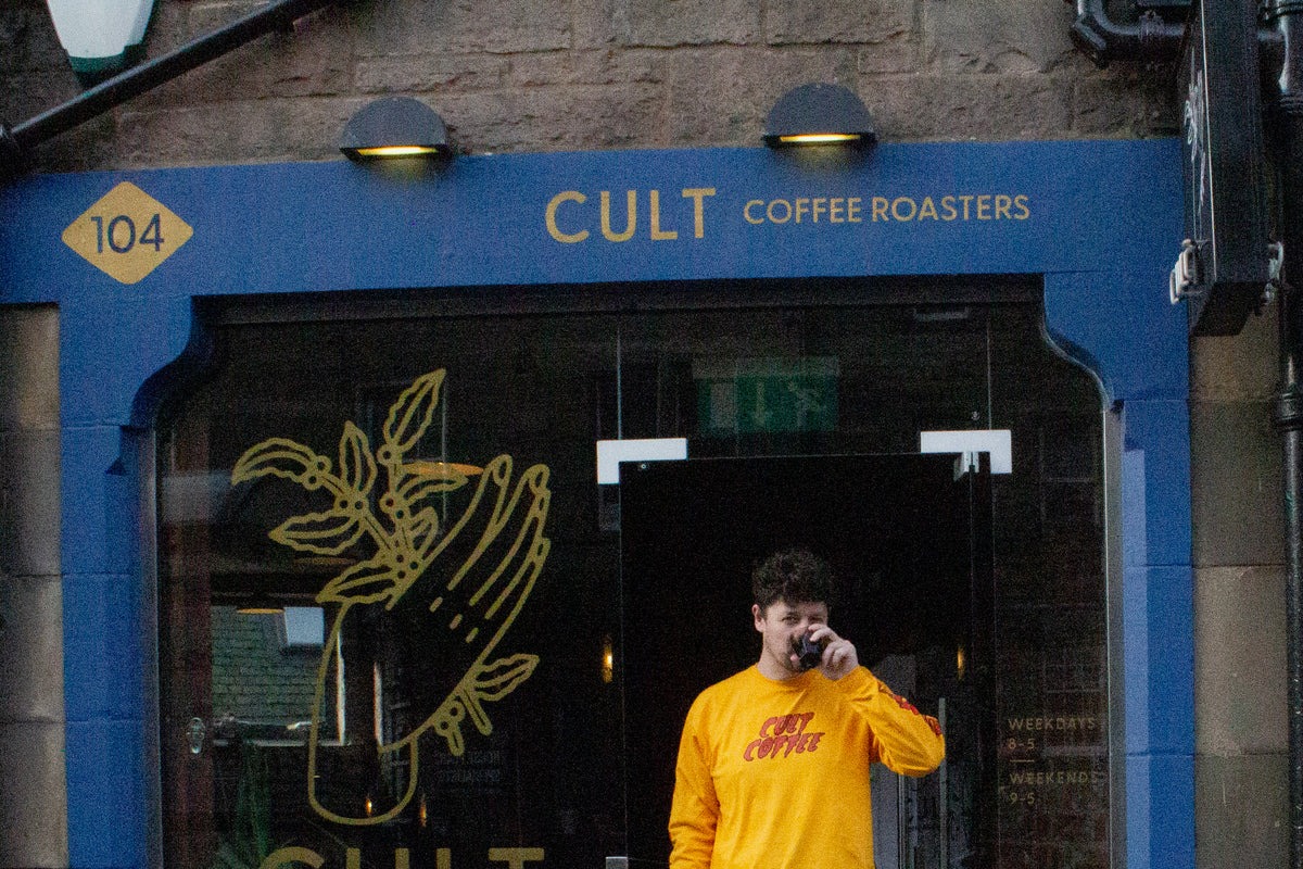 Cult Coffee Roasters' blue shopfront at number 104 with gold CULT COFFEE ROASTERS lettering, a hand drawn coffee plant decal on the window, and posted weekday and weekend hours