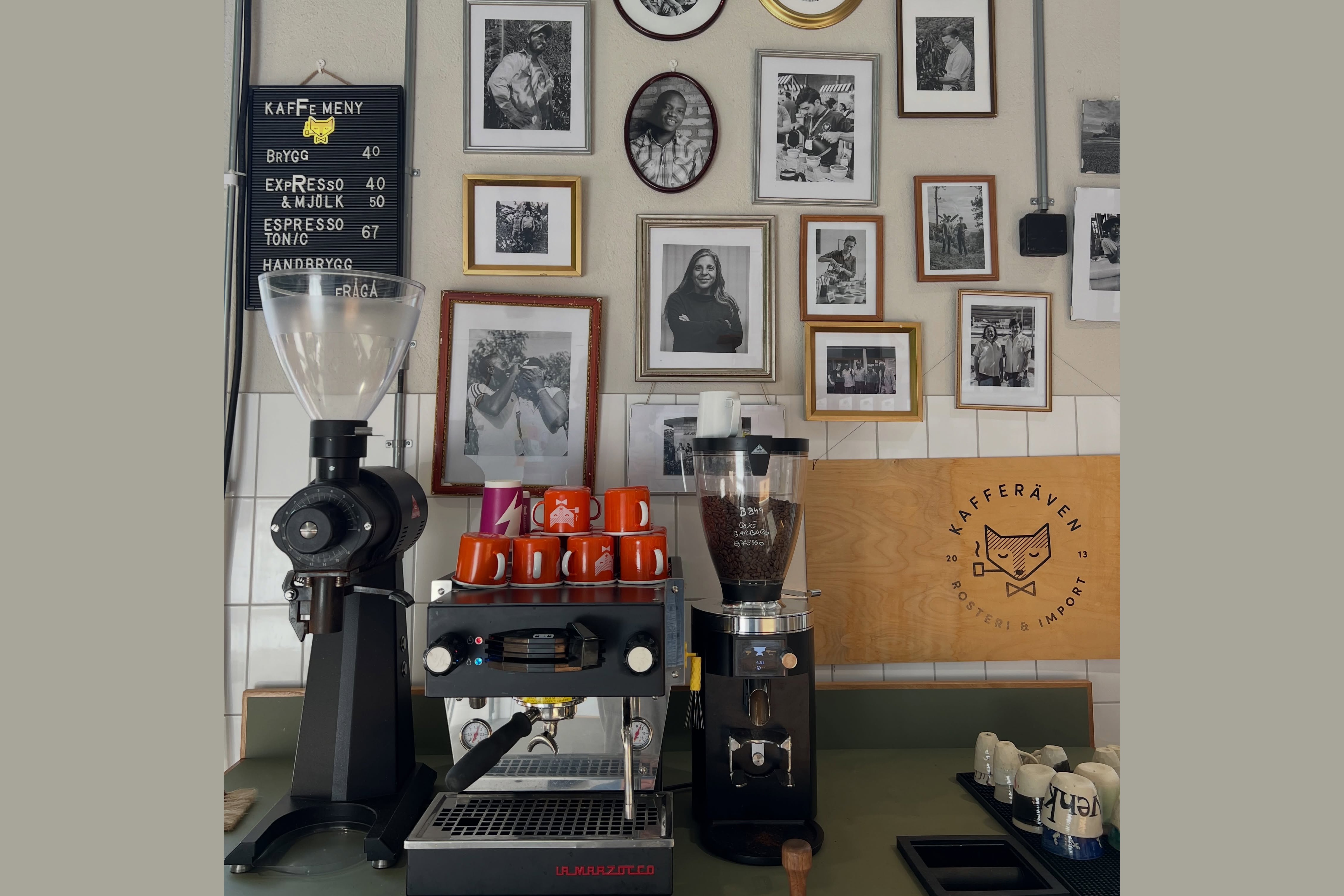 The espresso bar at Kafferäven with a La Marzocco machine, orange branded cups, and a wall of black and white producer portraits behind