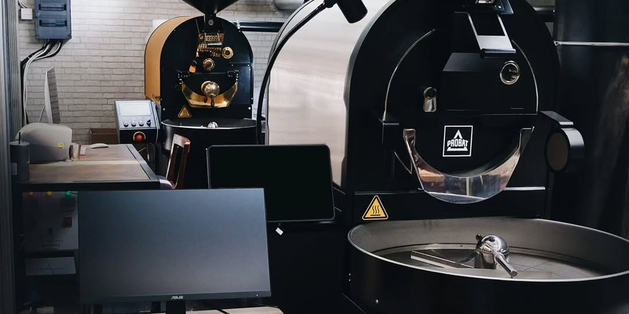 The roasting room at A Roastworks, a large Probat drum roaster beside a smaller machine, control panels and monitors on the counter in front