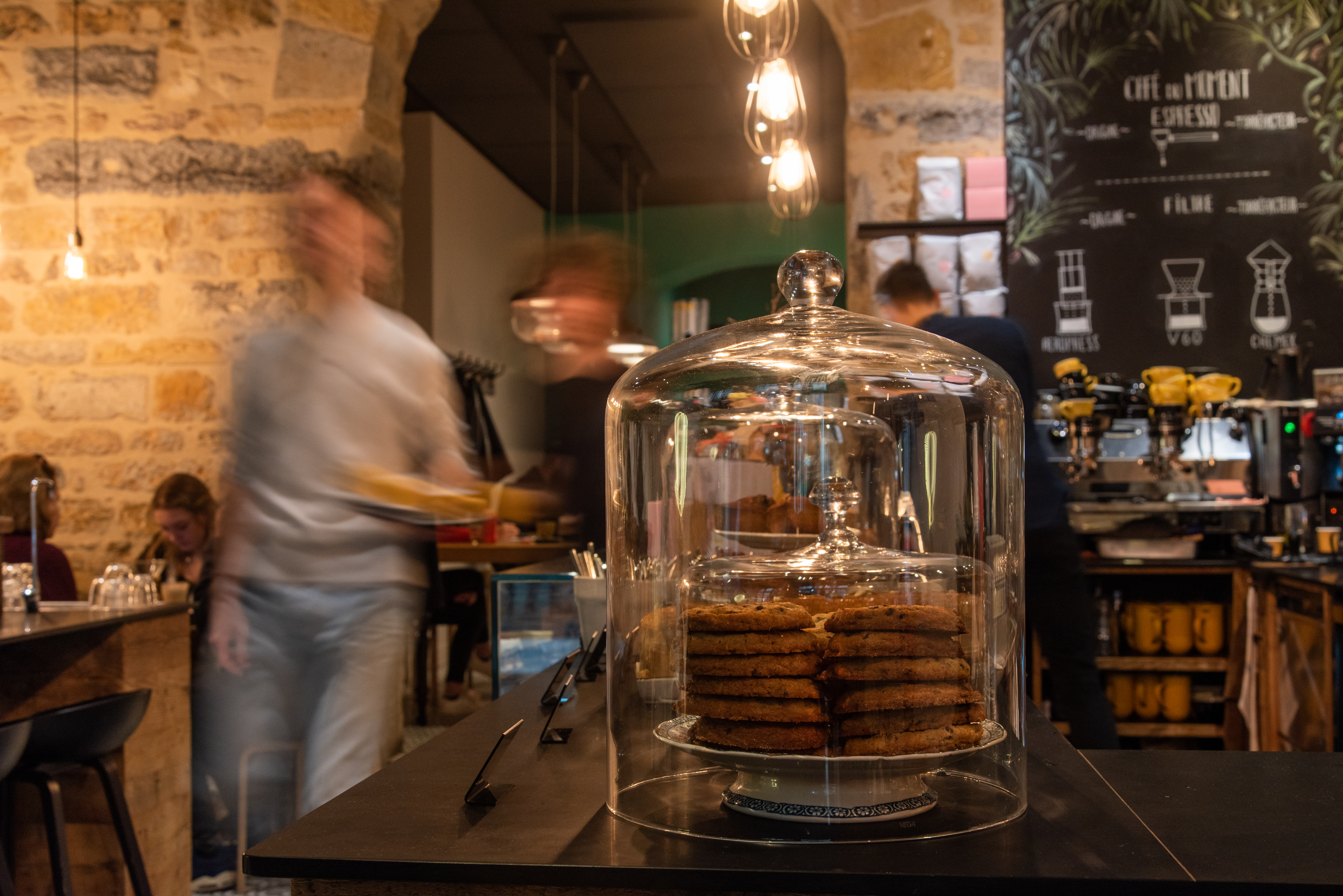 The stone vaulted interior of Slake with a stack of cookies under a glass cloche on the counter and the espresso bar behind