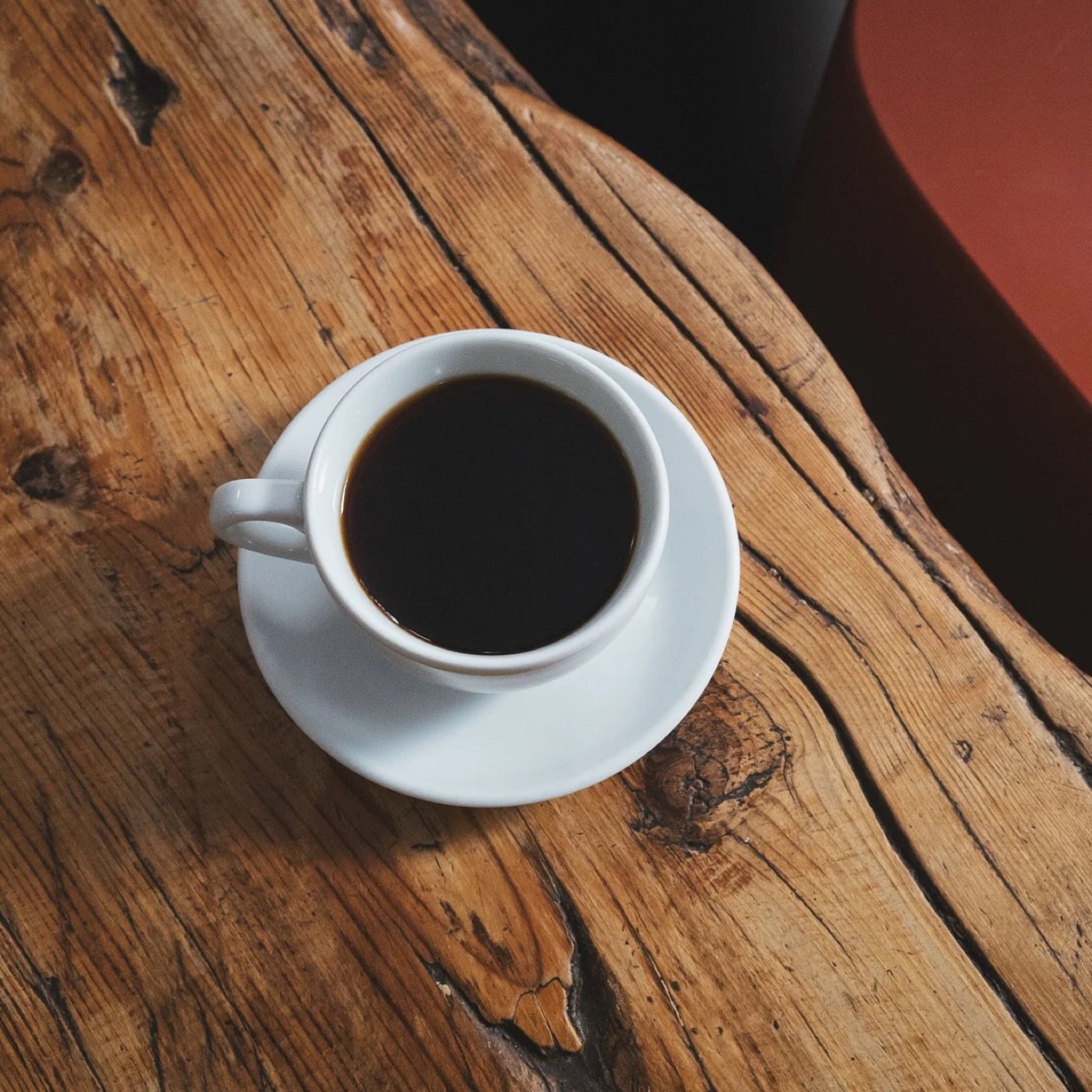 A cup of black coffee on a saucer set on a weathered wood table at Toma Cafe