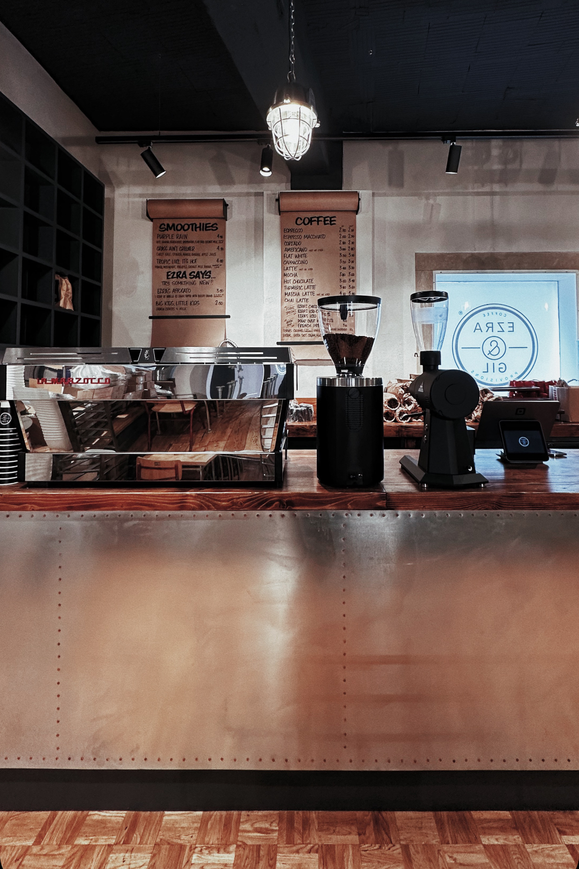 The counter at Ezra & Gil with an espresso machine, grinders, and the round Ezra & Gil logo etched on the window behind