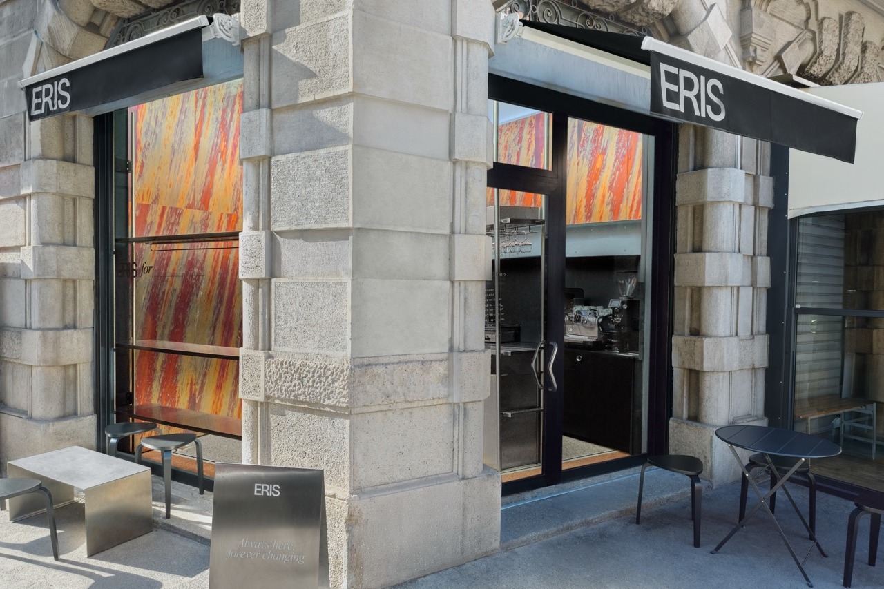 The Eris storefront with its current Naessi Studio mural in the windows, black ERIS awnings and outdoor tables against carved stone pillars