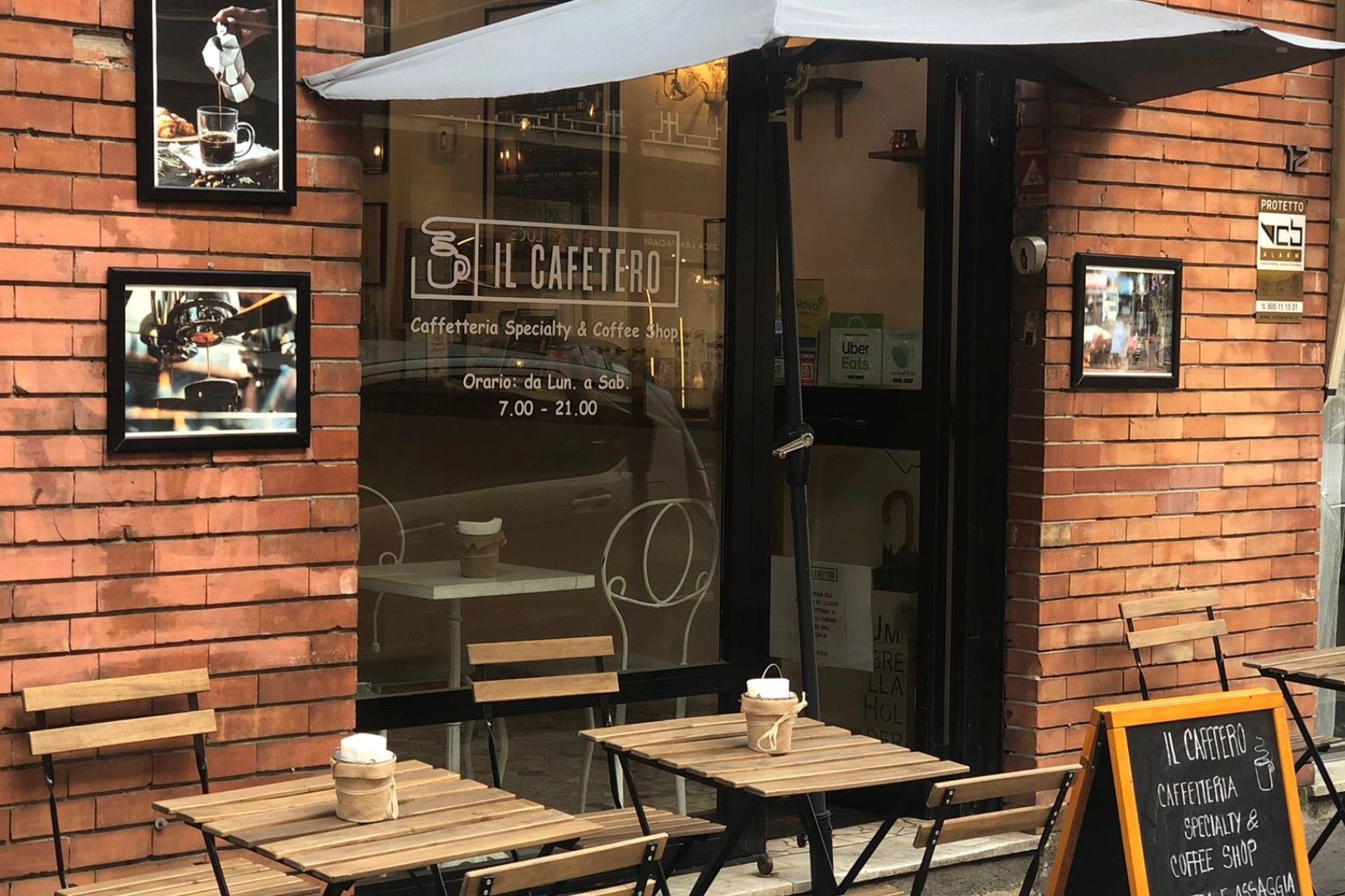 The IL CAFETERO storefront on the brick corner, framed coffee photos on the wall and outdoor tables beneath an umbrella