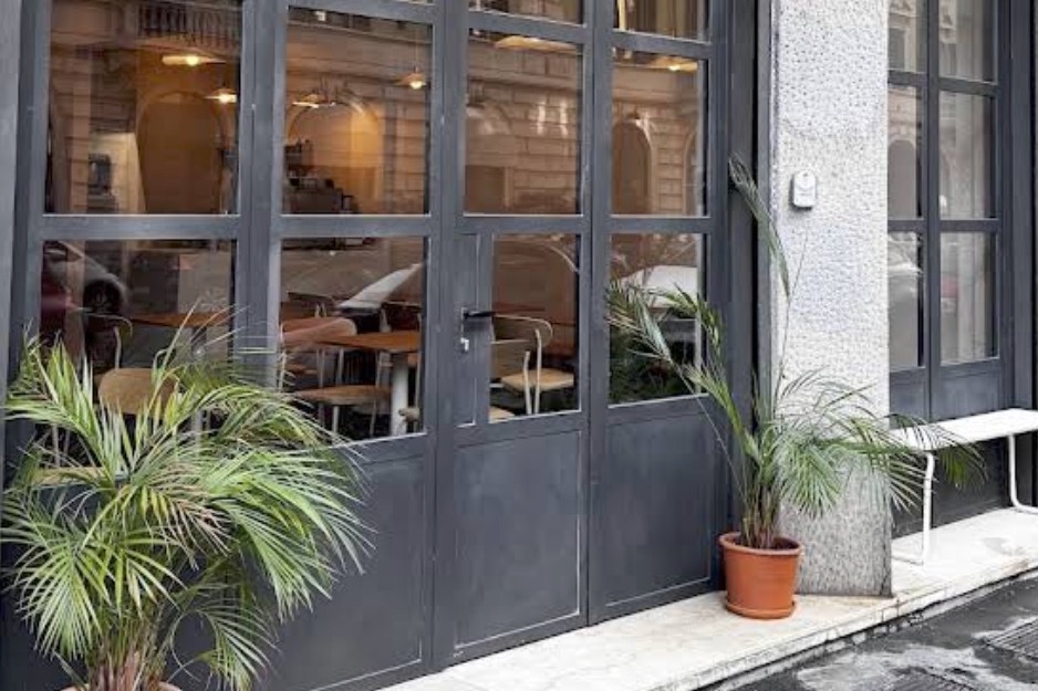 The June Collective storefront, black framed windows and doors with potted palms out front and wooden tables visible inside