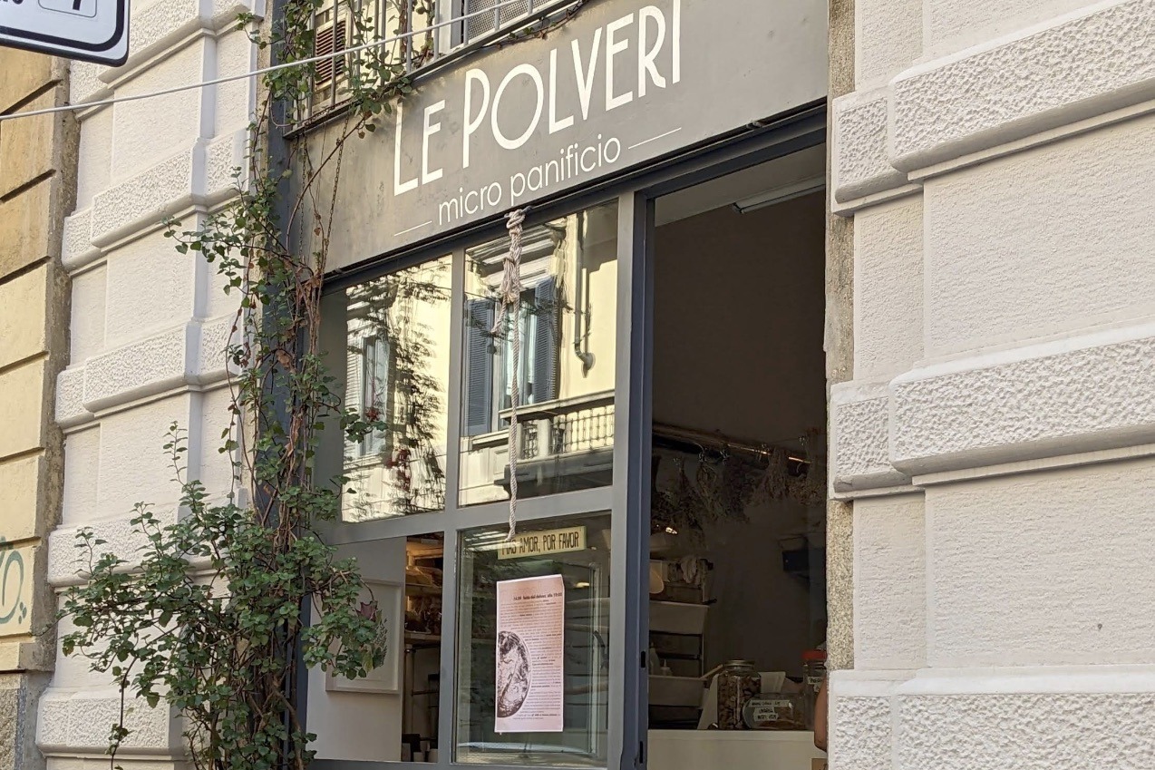 The LE POLVERI micro panificio sign above the storefront, climbing vines beside the open door and bakery shelves visible inside
