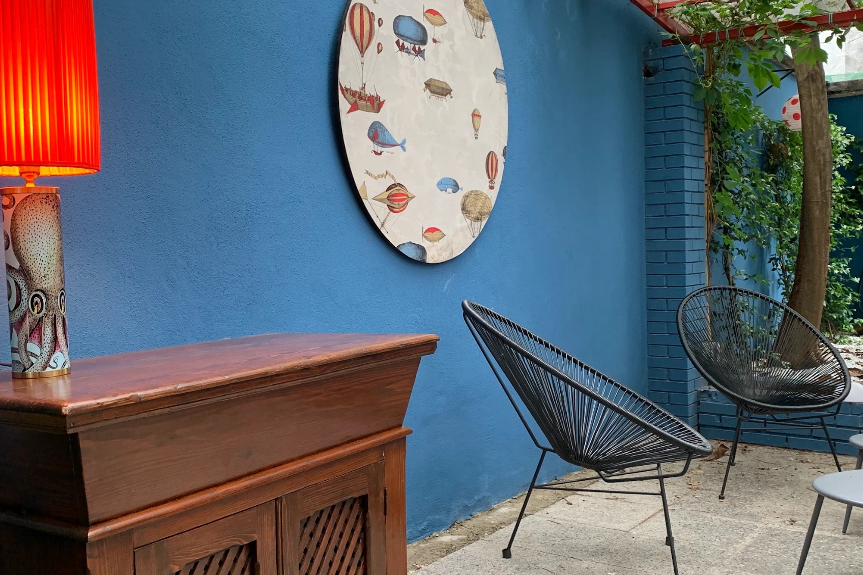 Onest's internal courtyard, black woven Acapulco chairs beside a blue wall hung with a round illustrated panel