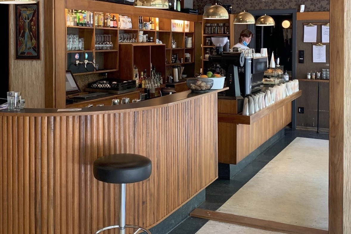 The curved fluted wood bar at Fuglen, brass dome pendant lights above vintage shelving and bottles, retail bean bags lined along the counter