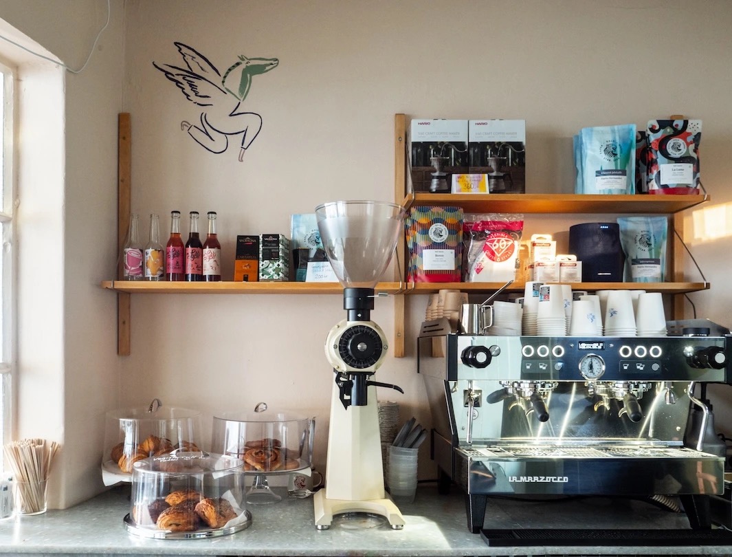 The espresso counter and pastry shelves inside Kiosk! in Oslo, with a small flying horse mural on the wall above