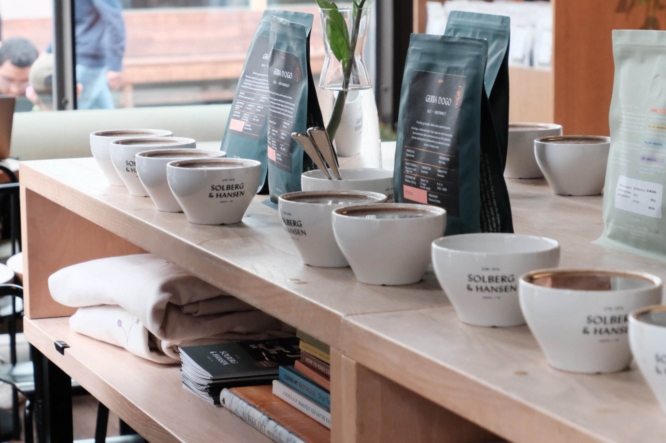 A cupping row of branded Solberg & Hansen bowls beside Gerba Dogo retail bean bags on the concept store's wooden counter