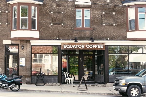 The Equator Coffee storefront at 412 Churchill Avenue North, a row of brick townhouses with large glass windows and a bistro table out front
