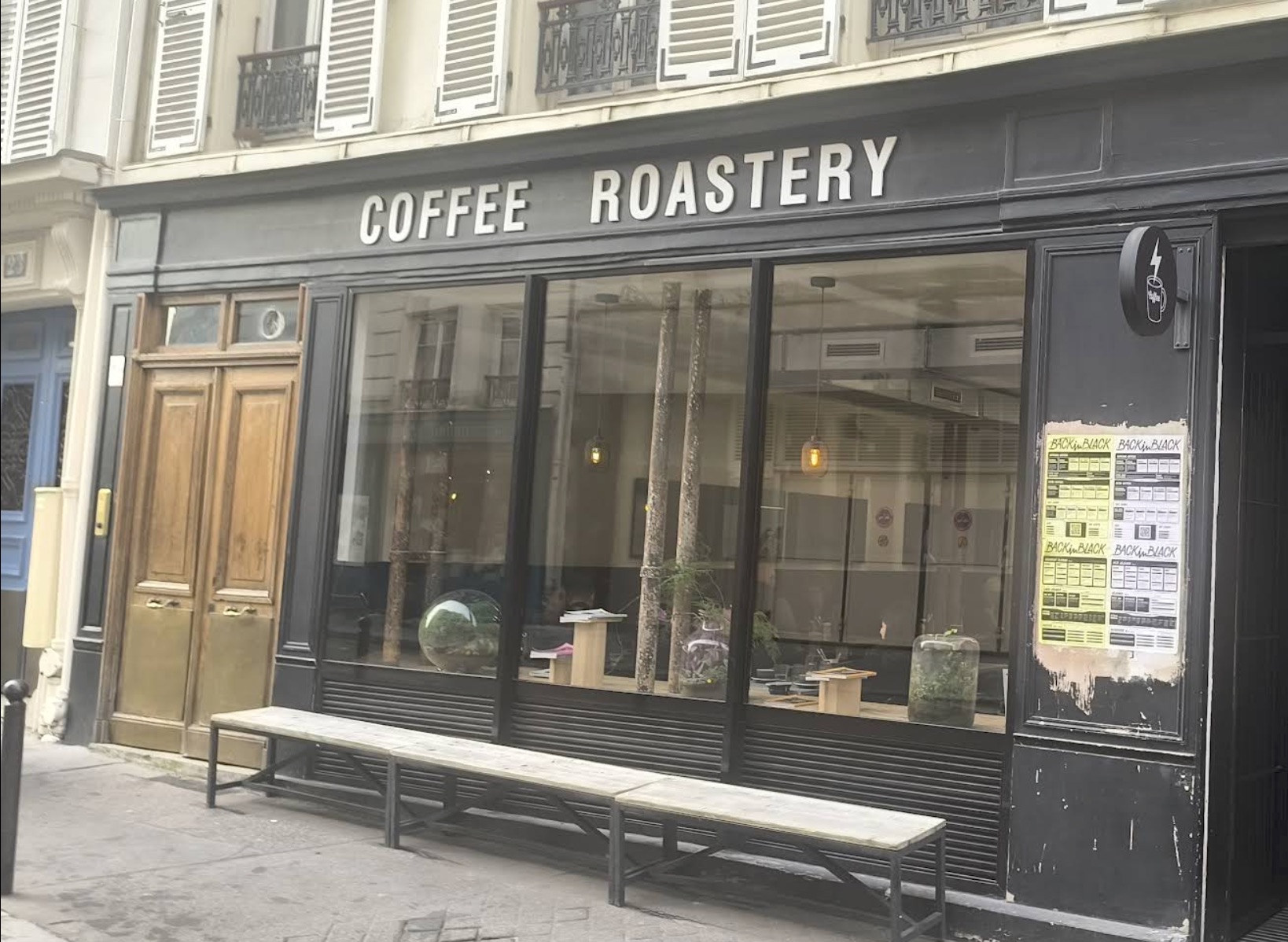 The black storefront of Back in Black on Rue Amelot, COFFEE ROASTERY lettered above tall windows, wooden benches along the pavement and menus posted beside the door