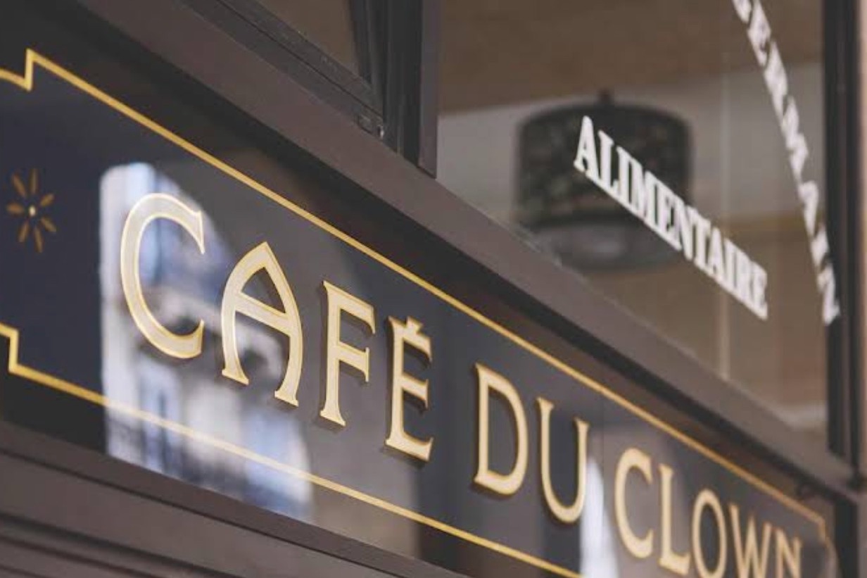 The Café du Clown sign in gold lettering on the storefront glass, with the arched Marché Saint-Germain Alimentaire lettering reflected above it