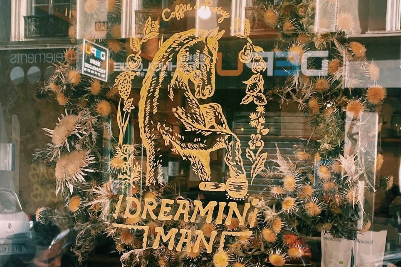 The gold horse and Dreamin' Man wordmark painted on the window at Rue Amelot, framed by a wreath of dried thistle and flowers