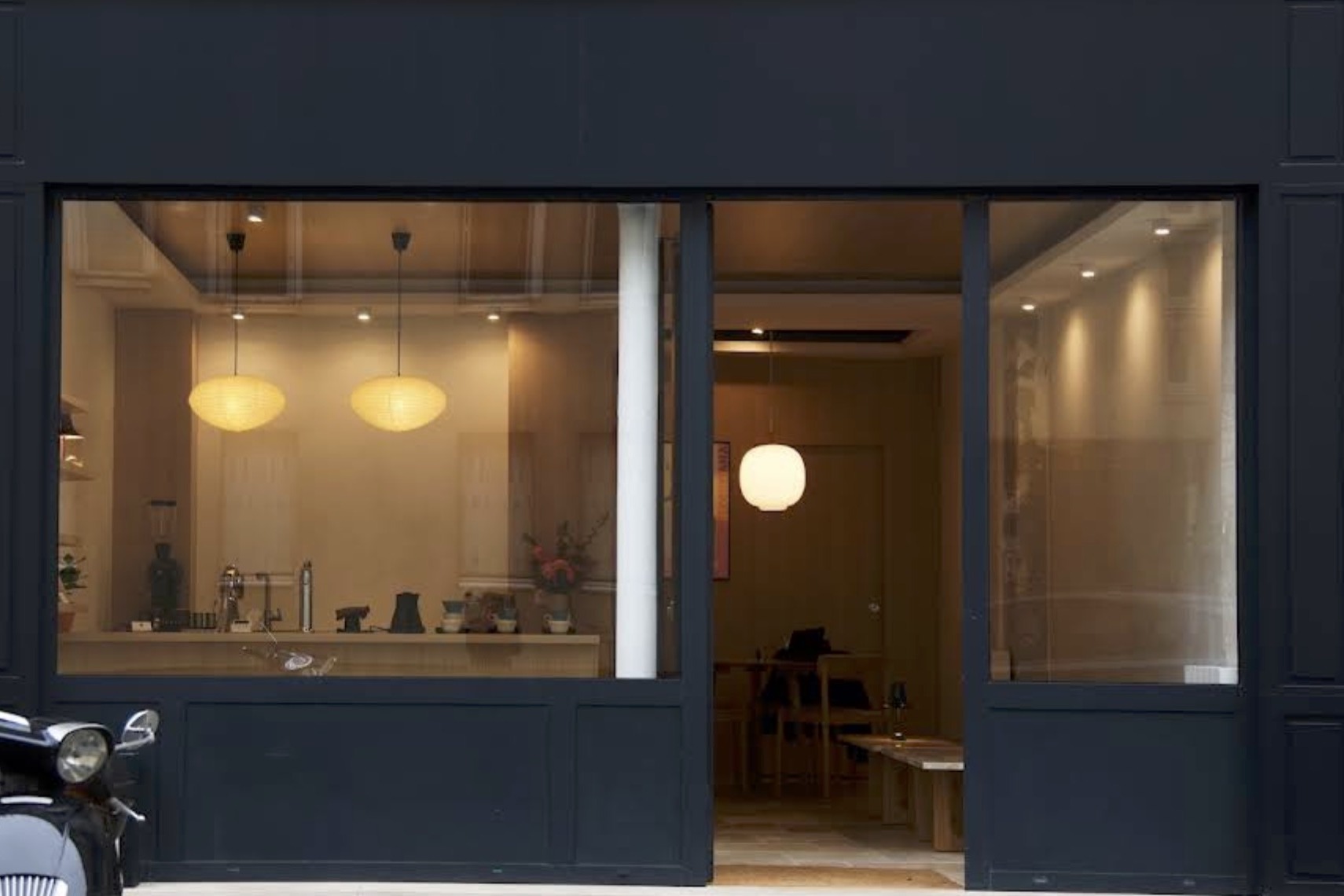 The dark navy Klover Coffee Showroom storefront at dusk, paper lantern lights glowing over the counter and a second room visible through the open door