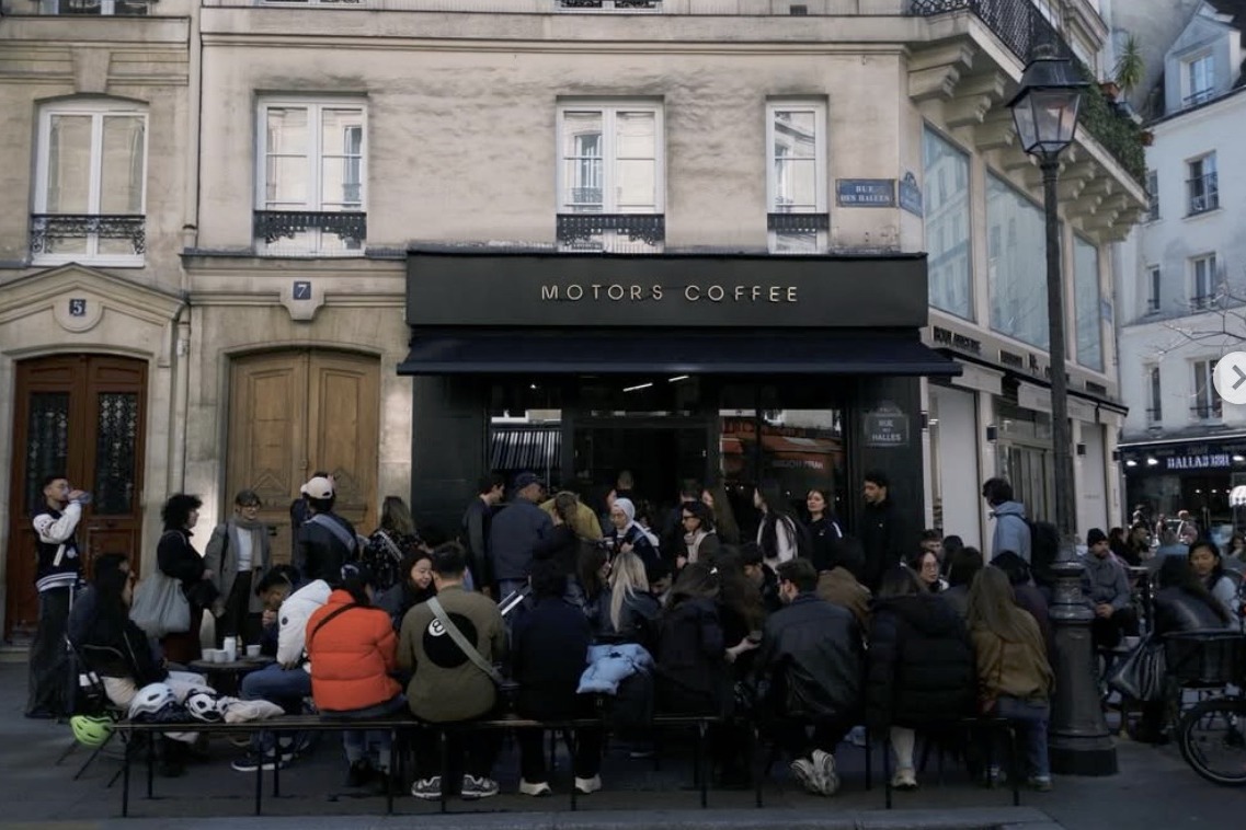 A crowd gathered outside Motors Coffee on the corner of Rue des Halles, the gold MOTORS COFFEE sign above the dark storefront
