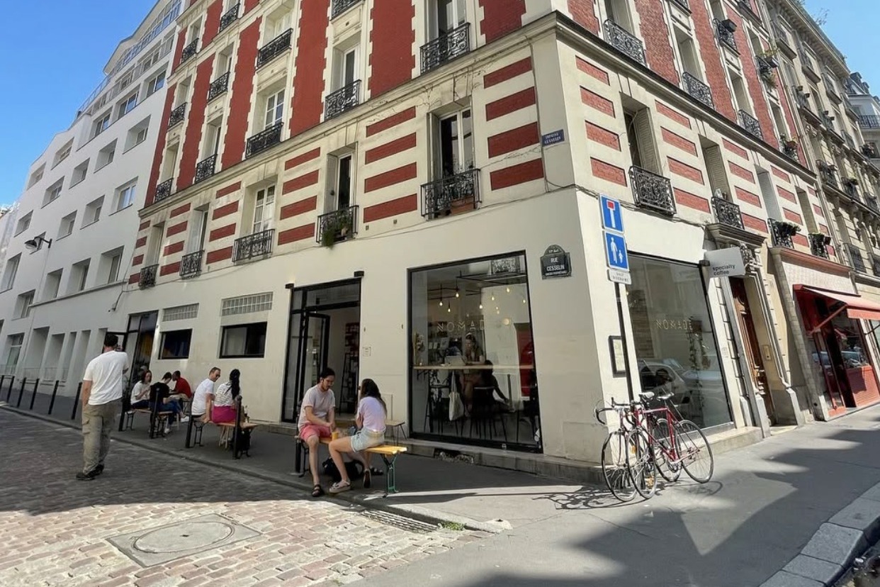 The corner storefront on Rue Paul Bert and Rue Cesselin, still signed Nomade, with customers seated at outdoor benches and bikes parked out front