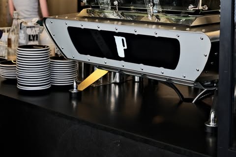 The roasting machine at Partisan Café Artisanal, its P logo panel beside stacked black and white striped saucers on the counter