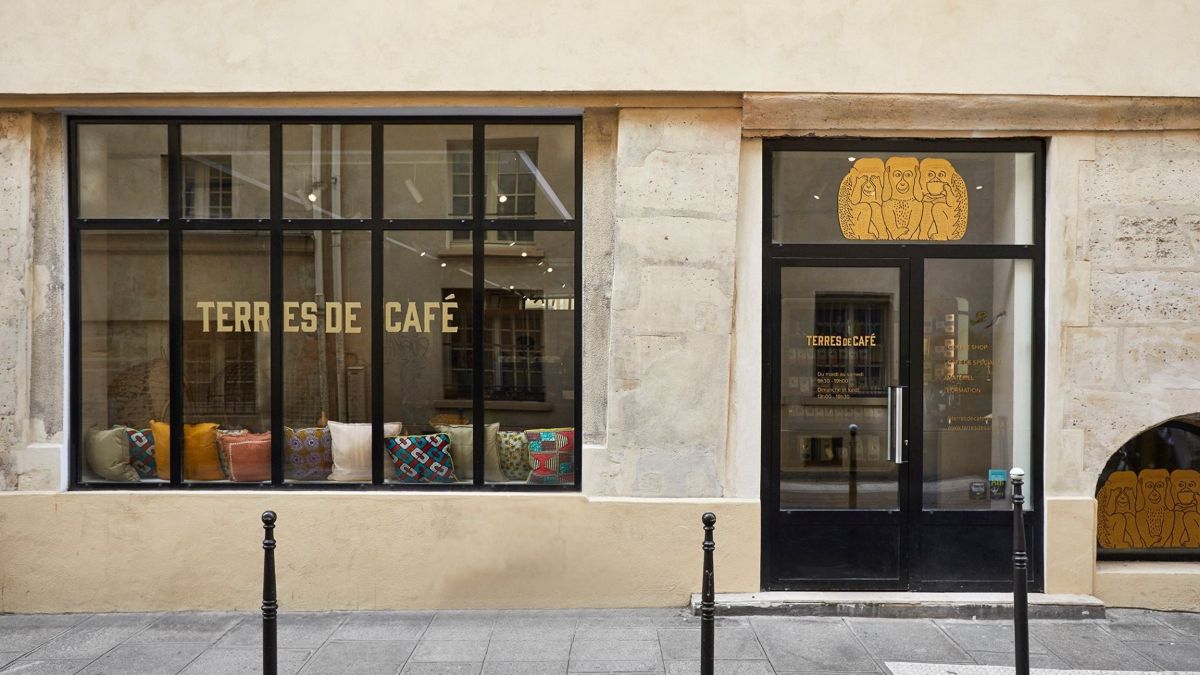 The Terres de Café storefront on Rue des Blancs Manteaux, gold lettering on black window frames and patterned cushions along the bench inside