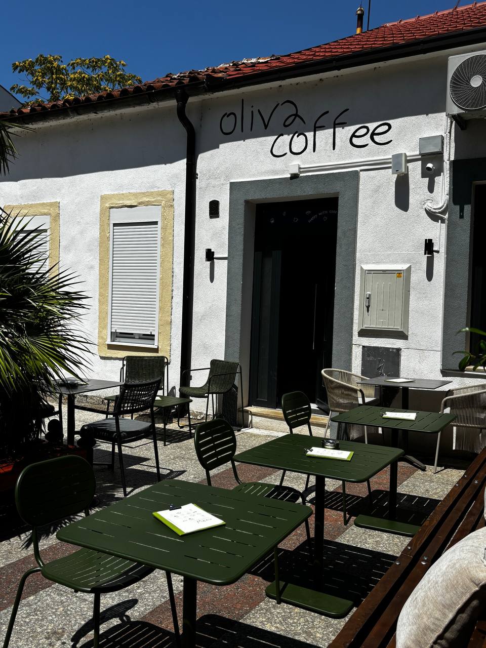 The stone facade of Oliva Coffee on Hercegovacka with its hand painted logo and outdoor terrace