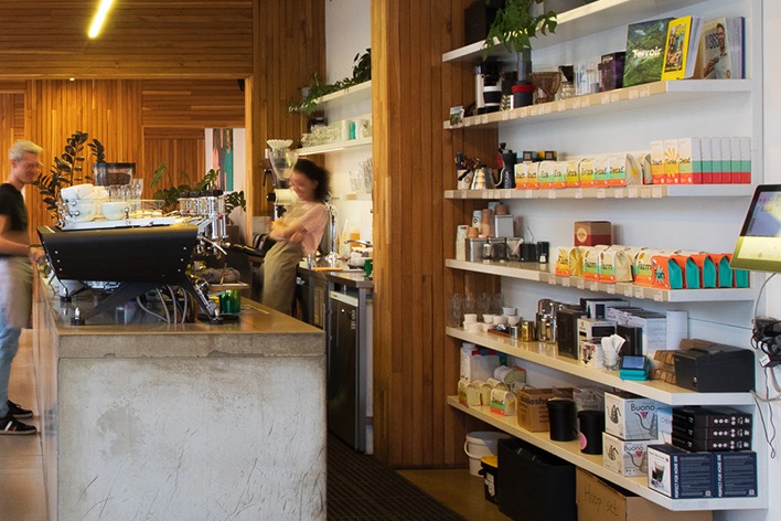The wood paneled counter at Doubleshot's Misto cafe with staff at work beside a wall of retail coffee bags and brewing gear