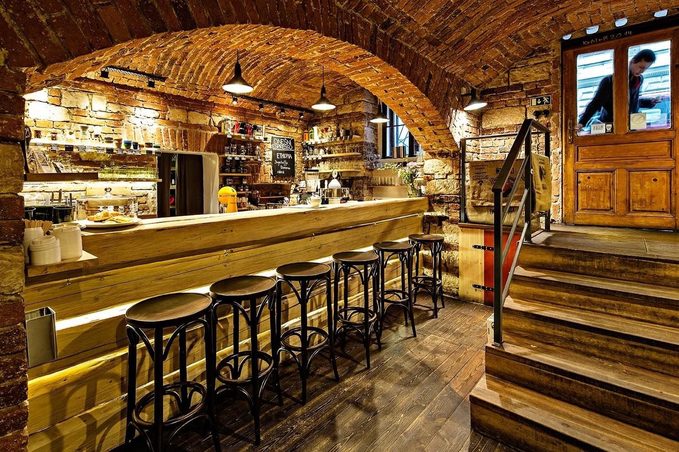 The brick vaulted cellar interior of Kavarna Prazirna with a wooden counter, bar stools and a small coffee roasting machine
